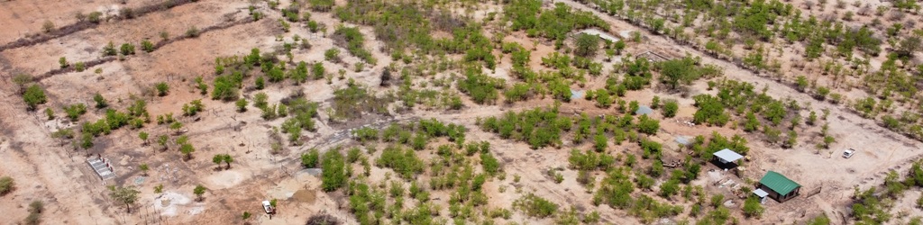 Aerial view of a farm with sandy brown soil and small green trees and shrubs. There are some farm buildings under construction and cleared areas for fields.